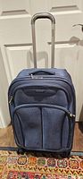 Front view of blue Samsonite suitcase showing wheels, zip pockets, handle retracted