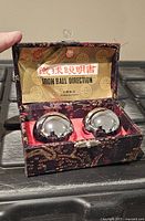 Open brocade box showing two polished metal Baoding balls and instruction sheet