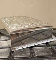 Closed silver-plated jewelry box on edge with tape measure showing width