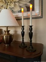 Two lit LED taper candles in bronze candlesticks on wooden surface