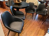 Four black faux leather chairs around a round table