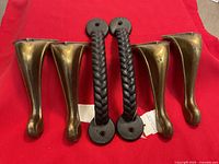 Two black braided metal handles and four bronze-tone footstool legs on red cloth