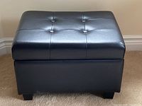 Front view of black faux leather ottoman showing tufted top and block feet