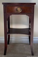 Front view of dark brown hardwood nightstand showing drawer with brass pull, lower shelf, curved legs