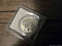 Obverse of coin showing Batman and Superman inside plastic sleeve