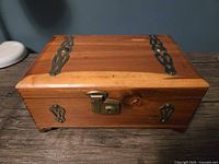 Front view of closed cedar box showing brass clasp lock and side straps