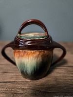 Front view of sugar bowl with lid on, showcasing handles and drip glaze