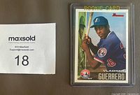 Front view of Vladimir Guerrero Sr. rookie card in protective sleeve beside lot number card