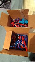 Two open cardboard boxes filled with assorted colored pens and visible blue USB chargers