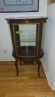 Full front view of curved glass display cabinet showing wood finish and glass panels