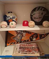 Shelf with Duke basketball, Ultra 94 basketball, Phillies cap, four baseballs, Flyers pennant and newspapers
