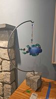 Full view of suspended glass fish on curved metal bar and stone base