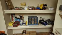Two shelves holding hardware cabinet, extension cords, brushes, tape, DAP tub, spray paint and packaged hardware