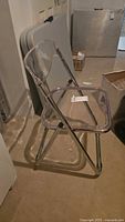 Single Lucite folding chair unfolded showing clear seat and back on chrome frame