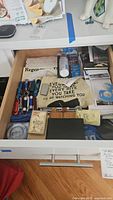 Open drawer showing multitools, flashlights, tea towel, letter openers, stationery