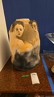 Full view of handmade pottery vase with sculpted faces and torsos