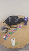 All four items on table: Timberland waist pack, Yeti mug in packaging, cooling scarf, purple Thermos tumbler