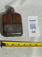 Front view of flask showing leather upper, silver plated lower beaker and cap alongside scale