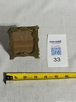 Front view of brass Art Nouveau miniature picture frame next to lot tag