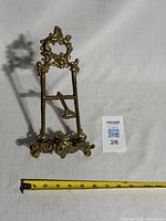Front view of ornate brass easel with measuring tape for scale