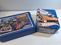 Two carrying cases closed: Matchbox vinyl case and Hot Wheels metal tin