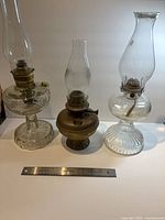 Three hurricane lamps side by side with ruler for scale