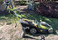 Side view of Radley electric lawn mower with attached grass bag and string trimmer leaning against handle