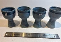 Front view of all four denim blue stoneware wine glasses with ruler for scale
