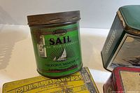 Green cylindrical Sail tobacco tin, part of yellow Millbank tin and green hinged tin visible