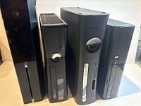 Four consoles standing vertically: Xbox One and three Xbox 360 units