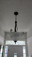 Chandelier hanging in hallway, full view with frosted glass bowl and metal scroll frame