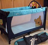 Travel cot assembled showing mesh sides, Pooh graphic, toy bar and mattress
