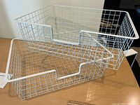 Two white wire baskets stacked showing grid construction and front cut-out