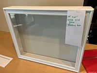 Front view of white wood and glass shadow box with dimension note