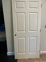 Full view of white six-panel door leaning against wall