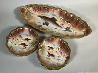 Oblong platter and two plates showing fish scenes and gilt scalloped rims