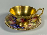 Teacup on saucer showing gold interior and fruit motif