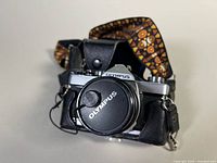 Front view of Olympus OM-1 camera with cap, case and strap