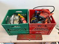 Two milk crates showing assorted power tools including belt sanders, saber saw and auger