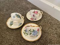 Three teacup and saucer sets showing floral patterns and gold gilt edges