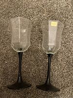 Two faceted clear bowl wine glasses with black stems on carpet