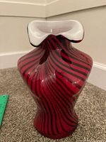 Front view showing red glass vase with black swirl stripes and white ruffled rim
