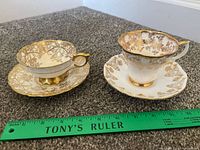 Two teacups and saucers on carpet with ruler for scale