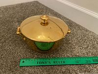 Top view of gold bone china casserole with lid beside ruler