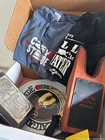 Box view showing t-shirts, boot jack, plate, metal case