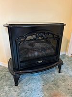 Front view of black cast iron style electric fireplace heater showing glass window, arched grill, simulated logs