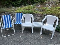 Full view of two white plastic patio chairs, white plastic side table, and two blue striped folding chairs