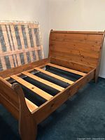 Full view of pine sleigh bed frame with mattress and box spring set aside