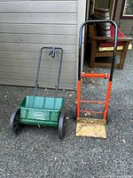 Scotts green hopper spreader and orange hand truck standing side by side for size and condition reference