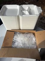 Stacks of white foam clamshell containers and box of plastic forks